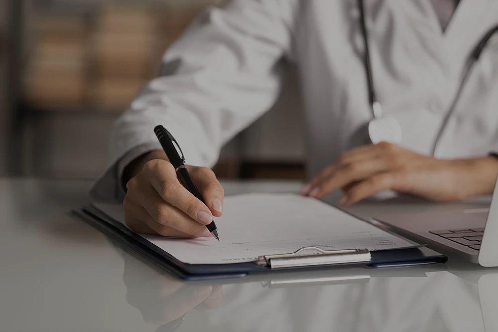 close up of a doctor writing on a form on a clipboard